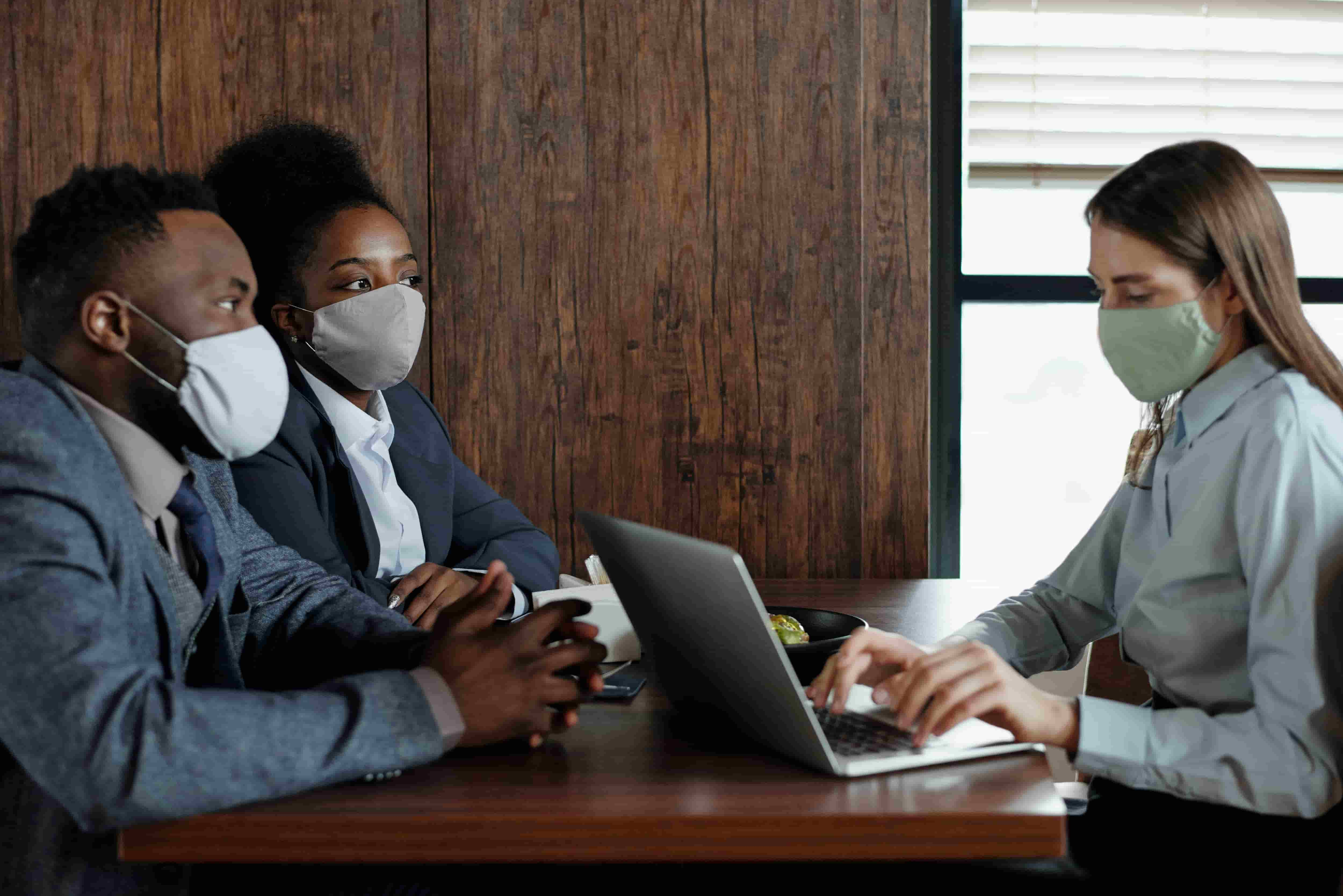 Man and woman with mask talking to another woman with mask who types on the computer