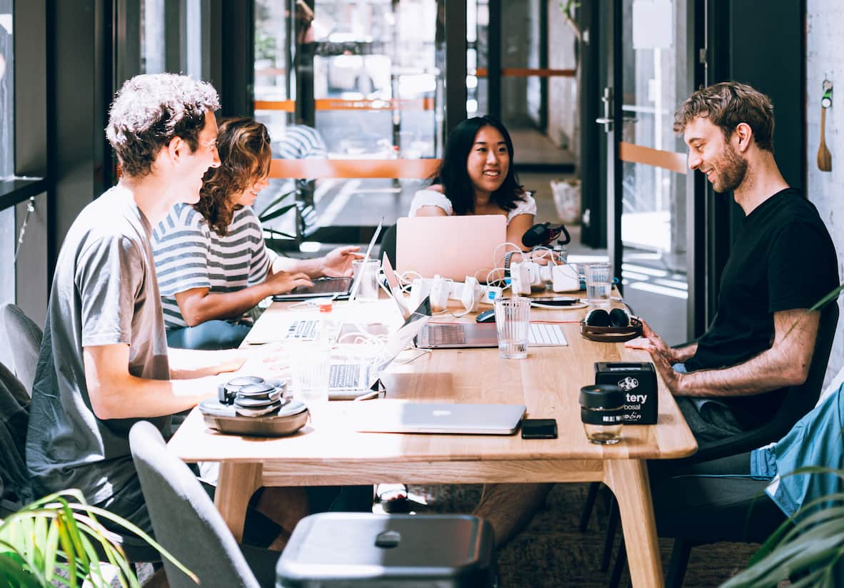 Equipo de cuatro personas trabajando con ordenadores en una mesa.